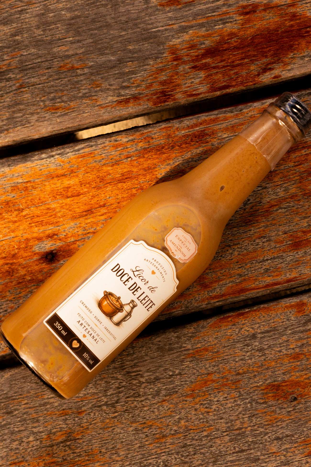 Garrafa da edição especial do licor de doce de leite com paçoca, sobre madeira rústica, com o selo Edição Especial com Amendoim